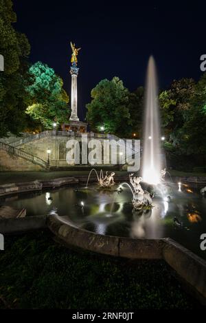 Fontana con getti d'acqua, sculture, scale e pilastro con l'angelo della pace nell'illuminazione notturna, Bogenhausen, Monaco, Germania Foto Stock