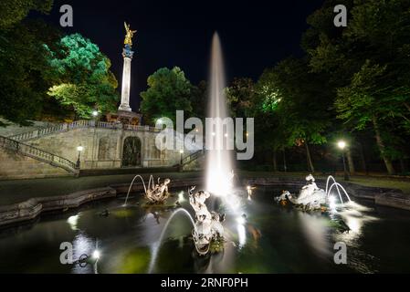 Fontana con getti d'acqua, sculture, scale e pilastro con l'angelo della pace nell'illuminazione notturna, Bogenhausen, Monaco, Germania Foto Stock