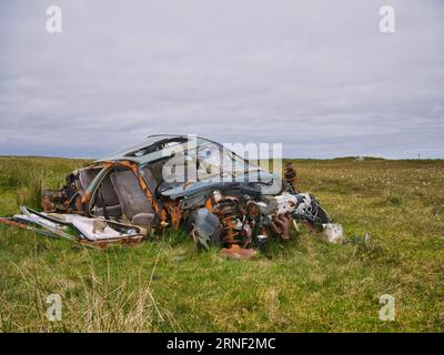 Un'auto spogliata, arrugginita e abbandonata su terreni agricoli rurali sull'isola di Benbecula nelle Ebridi esterne, Scozia, Regno Unito. Foto Stock
