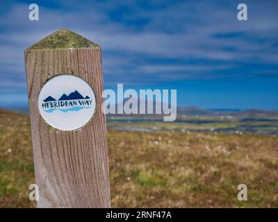 Un cartello bianco con stampa blu segna il percorso del sentiero Hebridean Way sull'isola di Benbecula nelle Ebridi esterne, Scozia, Regno Unito. Foto Stock