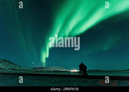 Un paio di viaggiatori stranieri guardano l'aurora boreale (aurora boreale) apparire nel cielo notturno a Hvalfjörður vicino a Reykjavik, in Islanda. Foto Stock