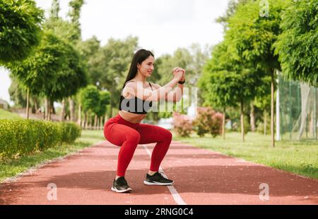 Bella donna che fa esercizio fisico la mattina all'aperto. fare squat in un parco all'aperto Foto Stock