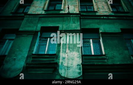 Una vecchia casa in pietra verde consumata con finestre adornate con tende bianche. Storia, nostalgia, e forse il passare del tempo. Foto Stock