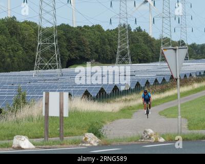 Grande fattoria solare a Vlissingen, Zelanda, Paesi Bassi, con ciclista su pista ciclabile e linee elettriche ad alta tensione. Foto Stock