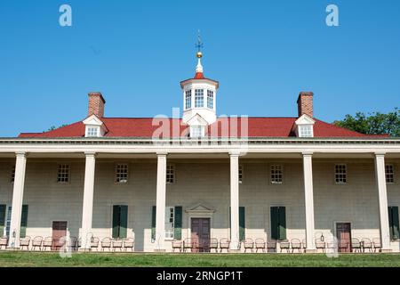 MOUNT VERNON, Virginia - l'esterno della residenza di George Washington di Mount Vernon si erge su un cielo azzurro. La struttura in legno a due piani, dipinta di bianco con persiane verdi, presenta la sua caratteristica piazza colonnata di fronte al fiume Potomac. Prati e giardini ben curati circondano la dimora storica. Foto Stock