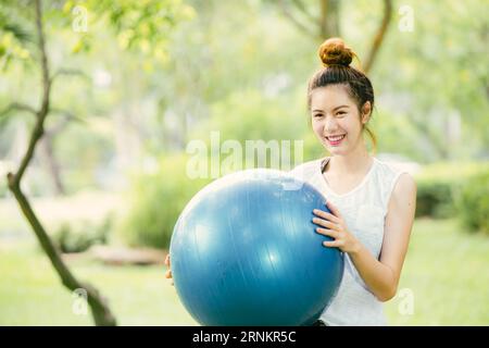 bella asiatica felice donna giocare divertirsi con la palla fitness esercizio al parco esterno sottile e sana ragazza attività di allenamento. Foto Stock