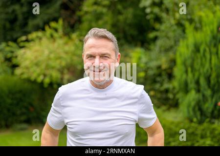 Ritratto della parte superiore del corpo di un attraente uomo di mezza età dei suoi 50 anni in piedi in giardino Foto Stock