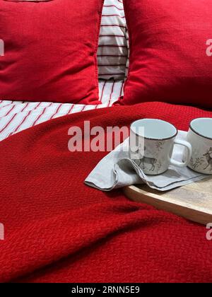 Lenzuola rosse. Vassoio in legno con tazze in ceramica sul letto. Colazione a letto. Materiali naturali in cotone e lino. Il romanticismo dell'amore. Tazze bianche Foto Stock