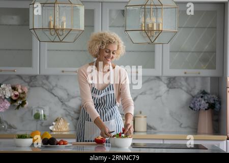 Allegra, positiva, una cuoca piuttosto matura che indossa il grembiule Foto Stock