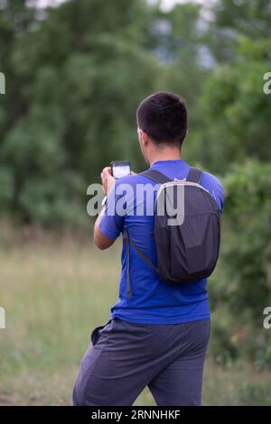 Foto professionale di un giovane uomo con zaino in natura che scatta foto con il suo telefono. Primo piano di un escursionista che scatta foto di una splendida natura Foto Stock