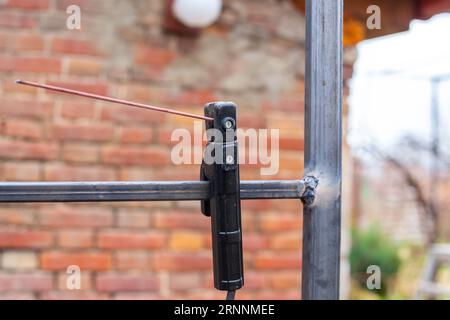 Trellis per uva proveniente da un tubo profilato saldato mediante saldatura elettrica, vicino alla casa. L'elettrodo di saldatura è fissato al tubo. Foto Stock