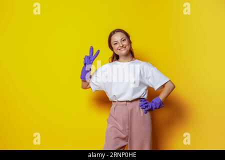 Happy Pretty Woman con guanti blu su sfondo arancione, servizio di pulizia e concetto di pulizia Foto Stock