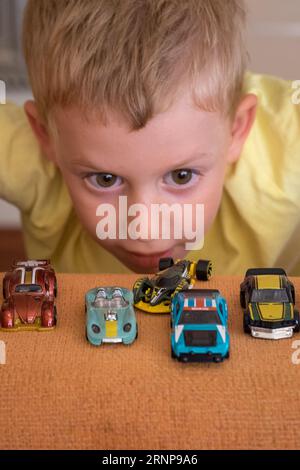 Un bambino carino che guarda e gioca con le sue auto a ruote calde Foto Stock