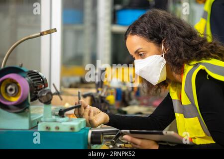 donna lavoratrice che lavora in officina dell'industria dei metalli pesanti che indossa una maschera facciale per l'igiene e la sicurezza Foto Stock