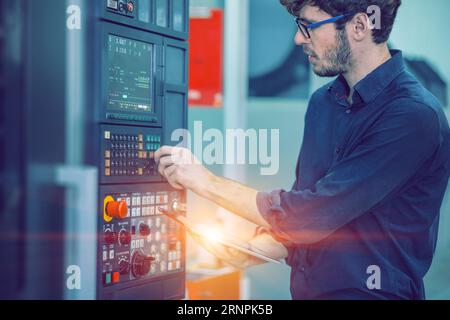 il giovane ingegnere maschio addetto al lavoro controlla la macchina moderna nella fabbrica di automazione. Tornio CNC in metallo Foto Stock