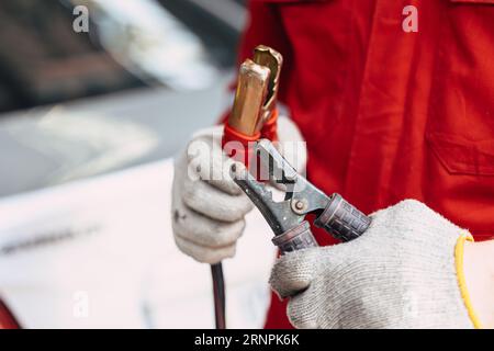 closeup maschio meccanico che fissa i morsetti della batteria impugnatura per caricare la batteria dell'auto in officina di riparazione automatica Foto Stock