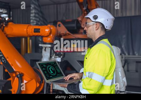 ingegnere maschio che utilizza il controllo del computer portatile aziona la macchina con braccio robotico industriale. manutenzione di controllo del test robotico di saldatura con programmazione man Foto Stock