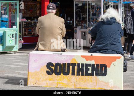 Coppia senior seduta su un blocco di cemento decorato sulla Marine Parade nelle gallerie di divertimento esterne a Southend on Sea, Essex, Regno Unito, in una calda giornata di sole Foto Stock