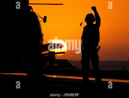 Mar Mediterraneo, acque internazionali. 30 agosto 2023. Un marinaio della Marina degli Stati Uniti segnala un elicottero MH-60R Sea Hawk assegnato allo Spartans of Helicopter Maritime Strike Squadron, per il decollo al tramonto sul ponte di volo a bordo della portaerei classe Nimitz USS Gerald R. Ford operante nel Mar Mediterraneo orientale, agosto 30, 2023 al largo delle coste della Grecia. Credito: MC2 Nolan Pennington/U.S. Navy Photo/Alamy Live News Foto Stock