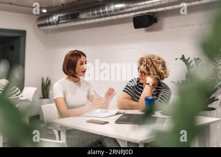 Colleghi di sesso femminile, giovani e anziani, riuniti a tavola in un'aula moderna. Foto Stock