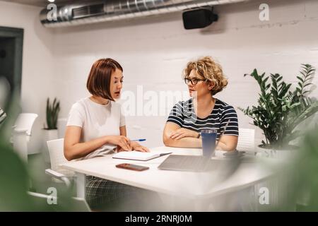 Educazione aziendale. I colleghi di lavoro junior e senior si riuniscono al tavolo in ufficio. Foto Stock