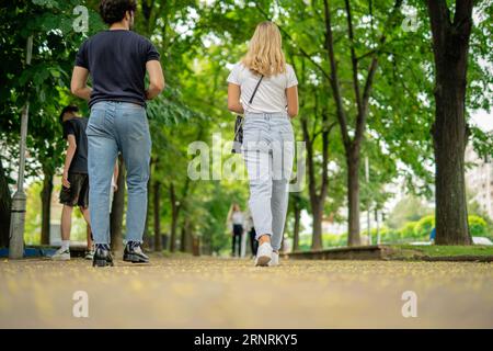 Foto con vista dall'angolo basso della coppia universitaria che torna a casa insieme dopo le lezioni, camminando sul marciapiede Foto Stock