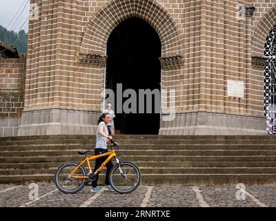 Jardín, Antioquia, Colombia - 4 aprile 2023: Passi giovani colombiani davanti alla Chiesa con una bicicletta Foto Stock