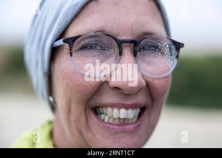 La donna con giacca impermeabile e gocce di pioggia sugli occhiali torna immersa in una passeggiata sul mare, Portbail, Cotentin, Manche, Normandia, Francia Foto Stock