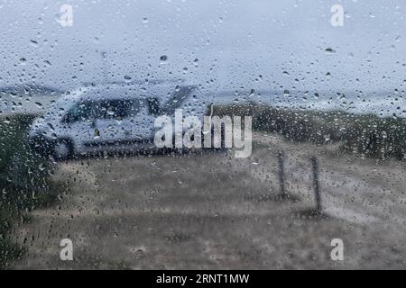 Vista di una casa mobile in riva al mare attraverso gocce di pioggia su una finestra, Portbail, Cotentin, Manche, Normandia, Francia Foto Stock