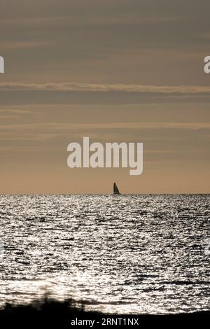 Barca a vela all'orizzonte con il mare scintillante e scintillante contro la luce del Canale della Manica poco di fronte a Portbail, Cotentin Foto Stock