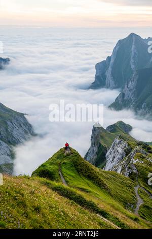 Due escursionisti che si godono la vista sulle montagne Saentis nella valle di Meglisalp all'alba, alta nebbia nella valle, Saentis, Appenzell Foto Stock