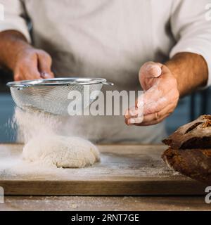 Panettiere setacciando la farina di grano con l'impasto impastato con setaccio in acciaio Foto Stock