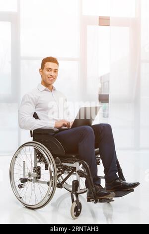 Ritratto disabile giovane uomo d'affari sorridente seduto su sedia a rotelle che utilizza l'ufficio del computer portatile Foto Stock
