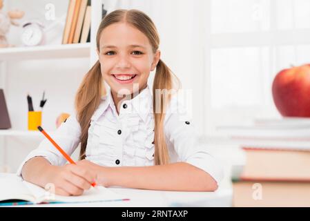 Sorridente bionda studentessa delle elementari che fa i compiti Foto Stock