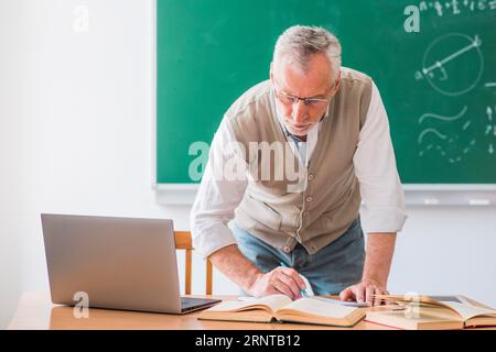 Insegnante di matematica senior che scrive con la penna mentre è in piedi contro la lavagna Foto Stock