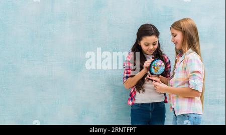 Sorridendo due ragazze in piedi contro la parete blu guardando piccolo globo Foto Stock