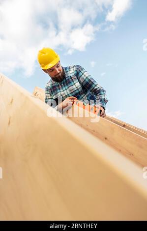 Lavoratore con elmetto controllo livello tetto casa in legno Foto Stock