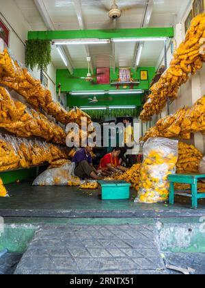 I fiori gialli si trasformano in Phuang Malai, le splendide ghirlande della cultura tailandese, sotto le dita agili di tre creatori a Bangkok. Foto Stock