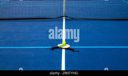 Due pagaie da picchiaduro e una palla a frusta gialla su un campo da picchiaduro e da tennis riverniciato e foderato. Foto Stock