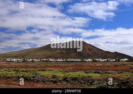 Paesaggio colorato e vulcano inattivo Montana Roja (montagna Rossa) con un piccolo villaggio alla sua base. Playa Blanca, Lanzarote, Isole Canarie, Spagna. Foto Stock