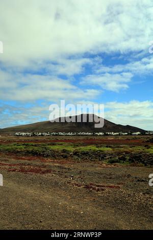 Paesaggio colorato e vulcano inattivo Montana Roja (montagna Rossa) con un piccolo villaggio alla sua base. Playa Blanca, Lanzarote, Isole Canarie, Spagna. Foto Stock