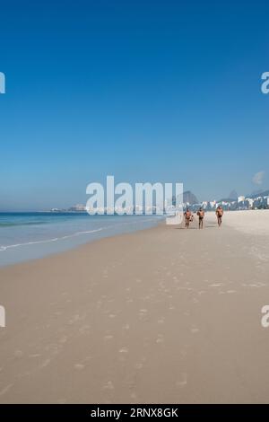 Rio de Janeiro, Brasile: Gente che fa jogging sulla sabbia della spiaggia di Leme con lo skyline della città e i suoi grattacieli lungo Avenida Atlantica (viale Atlantico) Foto Stock