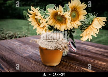 Bouquet di girasoli freschi e miele di girasoli in vasetti di vetro. Prodotti dell'apicoltura durante la raccolta del miele e la fioritura Foto Stock