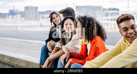 Un giovane gruppo di studenti felici seduti insieme fuori mentre uscivano Foto Stock