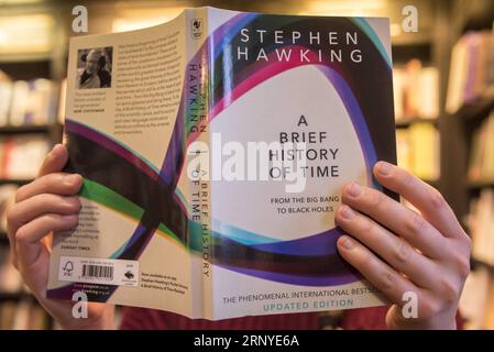 (180314) -- LONDRA, 14 marzo 2018 -- Un assistente di negozio posa con una breve storia del tempo, il libro più venduto del fisico di fama mondiale Stephen Hawking, in una libreria a Londra, in Gran Bretagna, il 14 marzo 2018. Il rinomato fisico britannico Stephen Hawking morì pacificamente a casa nella città universitaria britannica di Cambridge nelle prime ore di mercoledì all'età di 76 anni, ha detto il portavoce della sua famiglia). BRITAIN-LONDON-STEPHEN HAWKING-BOOKS StephenxChung PUBLICATIONxNOTxINxCHN Foto Stock