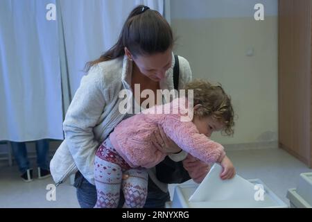 (180408) -- BUDAPEST, 8 aprile 2018 -- Una bambina aiuta sua madre a lanciare il voto in un collegio elettorale a Budapest, in Ungheria, l'8 aprile 2018. L'Ungheria ha iniziato le elezioni generali domenica per eleggere un parlamento di 199 seggi, il che potrebbe far sì che l'attuale primo ministro Viktor Orban abbia successo in un terzo mandato consecutivo. (Zxj) UNGHERIA-BUDAPEST-ELEZIONI PARLAMENTARI-VOTANTI AttilaxVolgyi PUBLICATIONxNOTxINxCHN Foto Stock