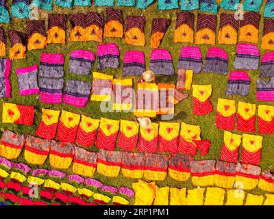Narayanganj, Dacca, Bangladesh. 3 settembre 2023. Centinaia di pezzi di stoffa tinta sono sparsi in un campo nel villaggio di Batik a Narayanganj, Bangladesh, per l'essiccazione che sembra un regno di colori. I lavoratori usano i cappelli per proteggersi dal calore bruciante perché devono girare costantemente i tessuti colorati in modo da asciugarsi perfettamente alla luce del sole. Tessuti colorati splendidamente decorati sono creati utilizzando la tecnica indonesiana chiamata ''Batik''. Le parti del progetto vengono bloccate applicando cera calda su di esse, quindi viene applicato un colorante sulla parte superiore e le parti coperte di cera resistono Foto Stock