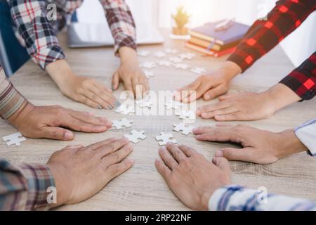 Gruppi di uomini d'affari che mettono le mani su un tavolo con puzzle. Concetto di cooperazione lavoro di squadra aiuto e supporto nelle imprese simboli di A. Foto Stock