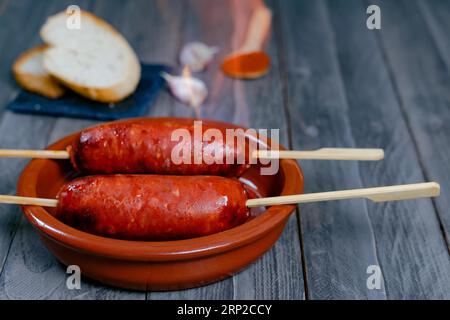 Chorizo grigliato, chorizo al infierno, in una pentola di argilla con pane, olive e paprika, un piatto tipico del cibo spagnolo Foto Stock