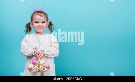 Piccola ragazza coniglietto orecchie che tiene un cestino con uova di pasqua Foto Stock